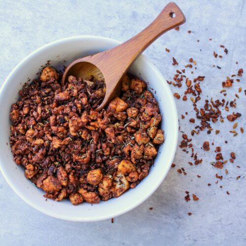 Vegan sausage crumbles in a white bowl with a wooden spoon.
