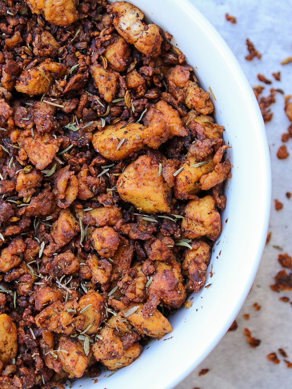 Vegan sausage crumbles with tofu, topped with thyme leaves, in a white bowl.