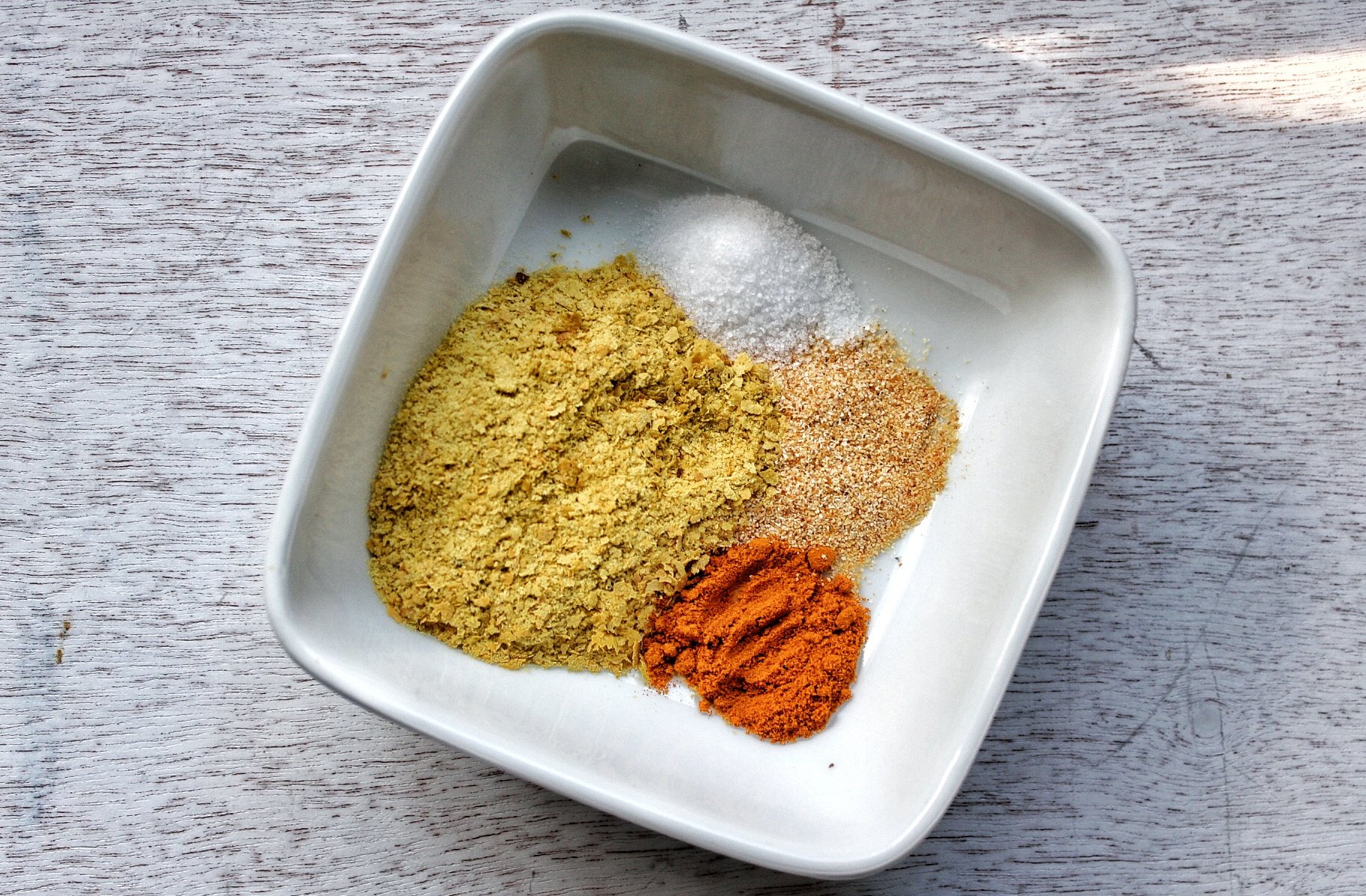 Nutritional yeast, salt, garlic powder, and turmeric in a small white glass bowl.