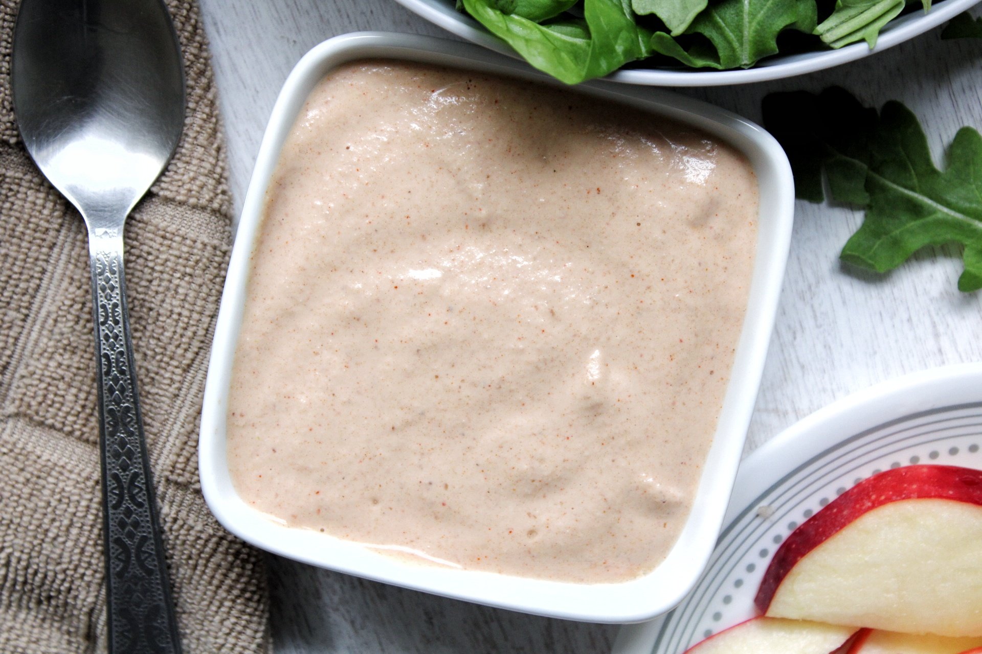 Small white bowl with creamy garlic salad dressing and side of green salad