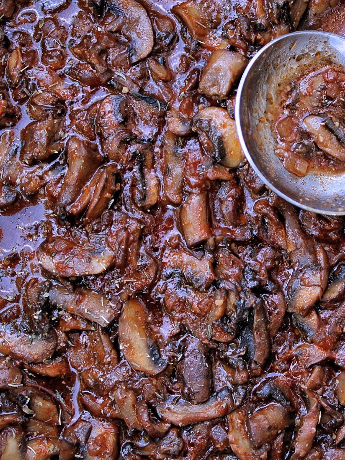 Closeup of braised mushrooms in a tomato sauce with a serving spoon.