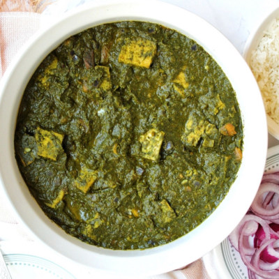 Vegan palak paneer in a large white bowl with a side of sliced onions and white rice.