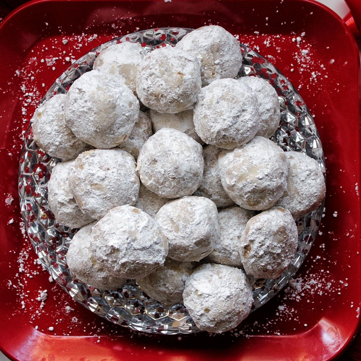Snowball cookies dusted with powdered sugar, plated a red and silver plate.