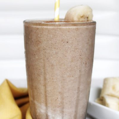 Milkshake in a glass cup with sliced banana and a yellow white stripped straw