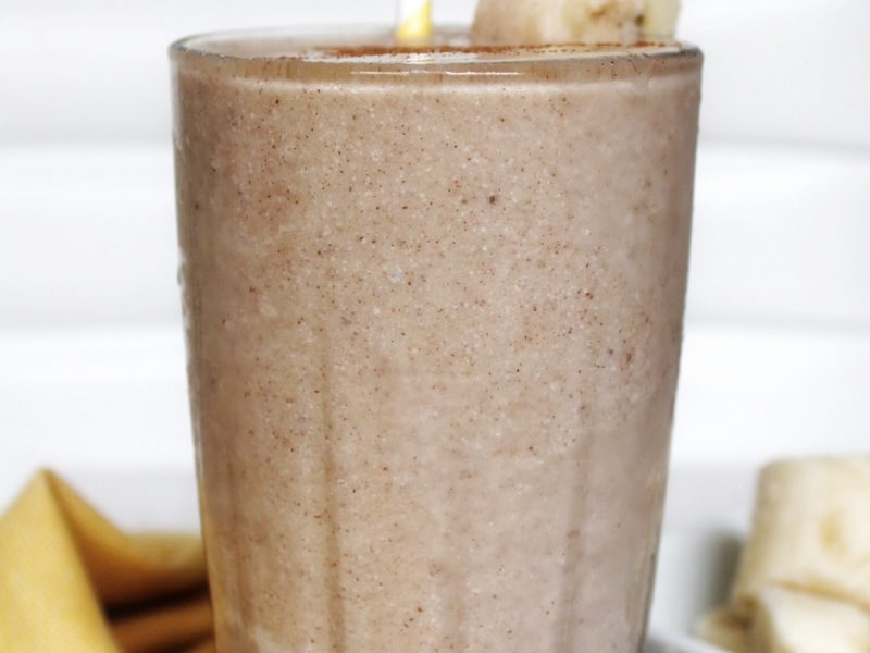 Milkshake in a glass cup with sliced banana and a yellow white stripped straw