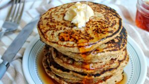 Stack of gluten-free oat bran pancakes topped with vegan butter and syrup.