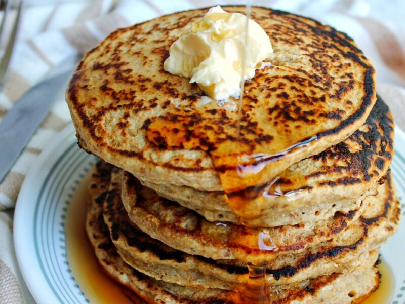 Stack of gluten-free oat bran pancakes topped with vegan butter and syrup.