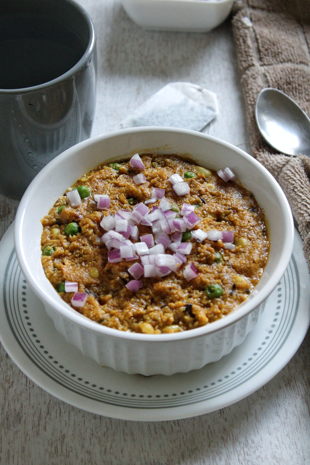 Cooked oat bran in a bowl topped with red onions and green peas.