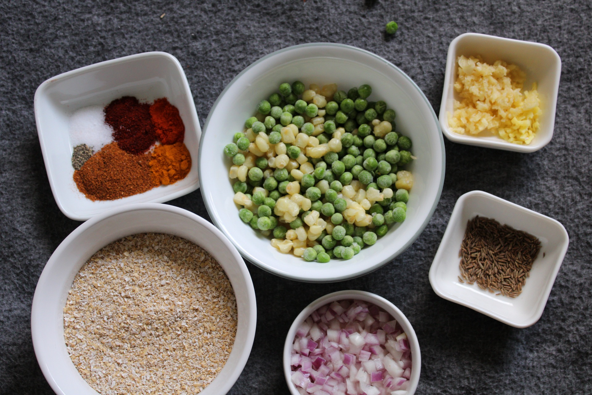 Frozen peas, frozen corn, garlic, cumin, onion, oats, and spices in small bowls 