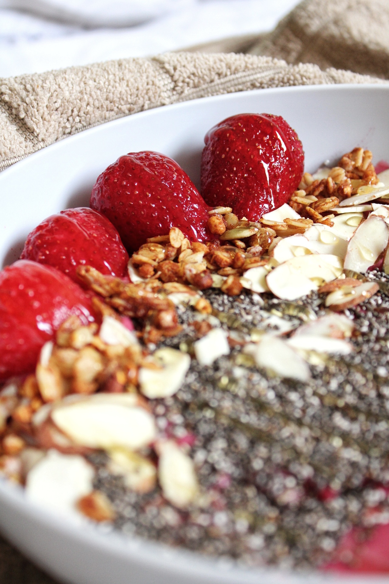 Strawberries, granola, almonds, and chia seeds topped over a raspberry smoothie bowl.