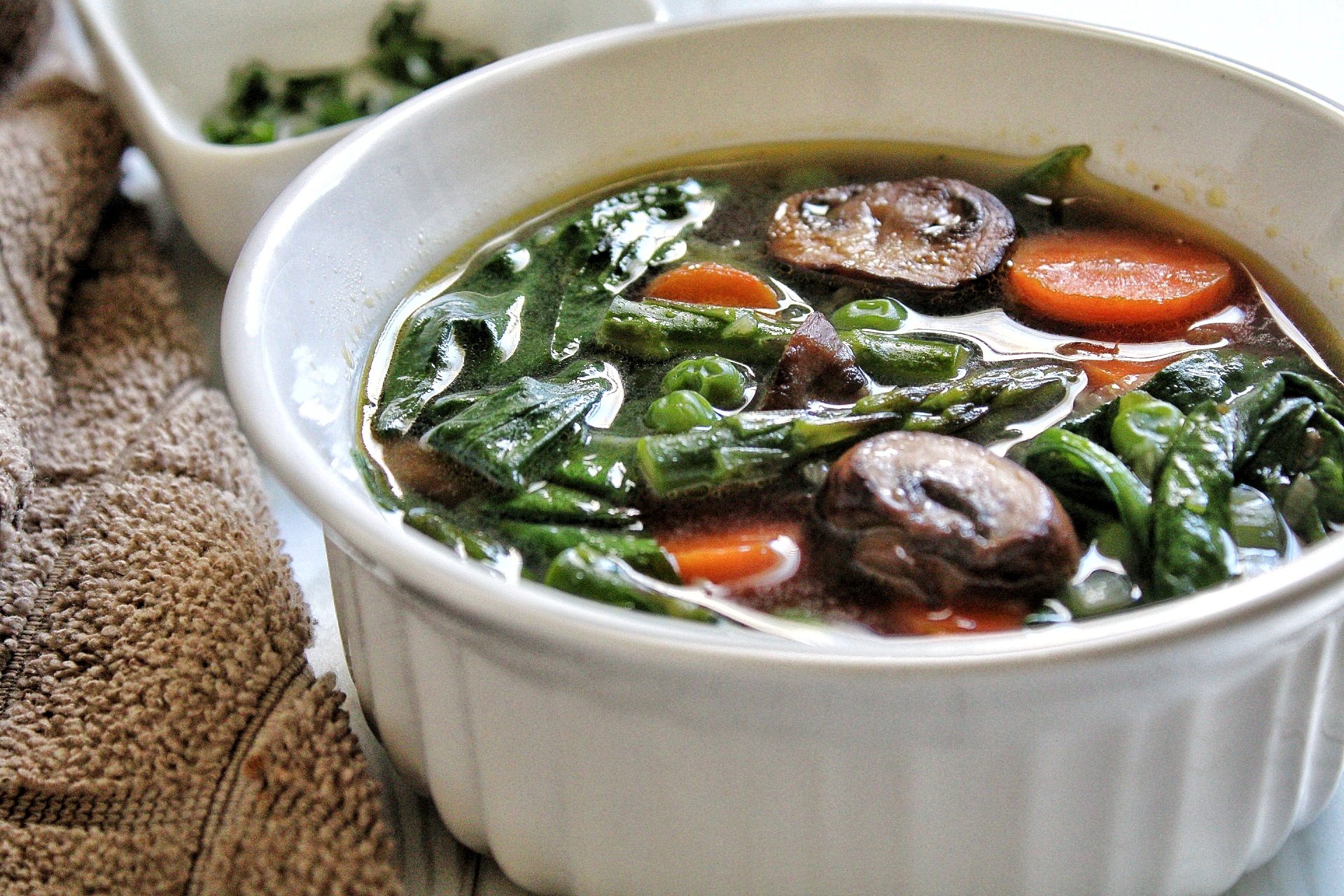 Spring soup with sliced carrots, mushroom, asparagus, and spinach in a bowl