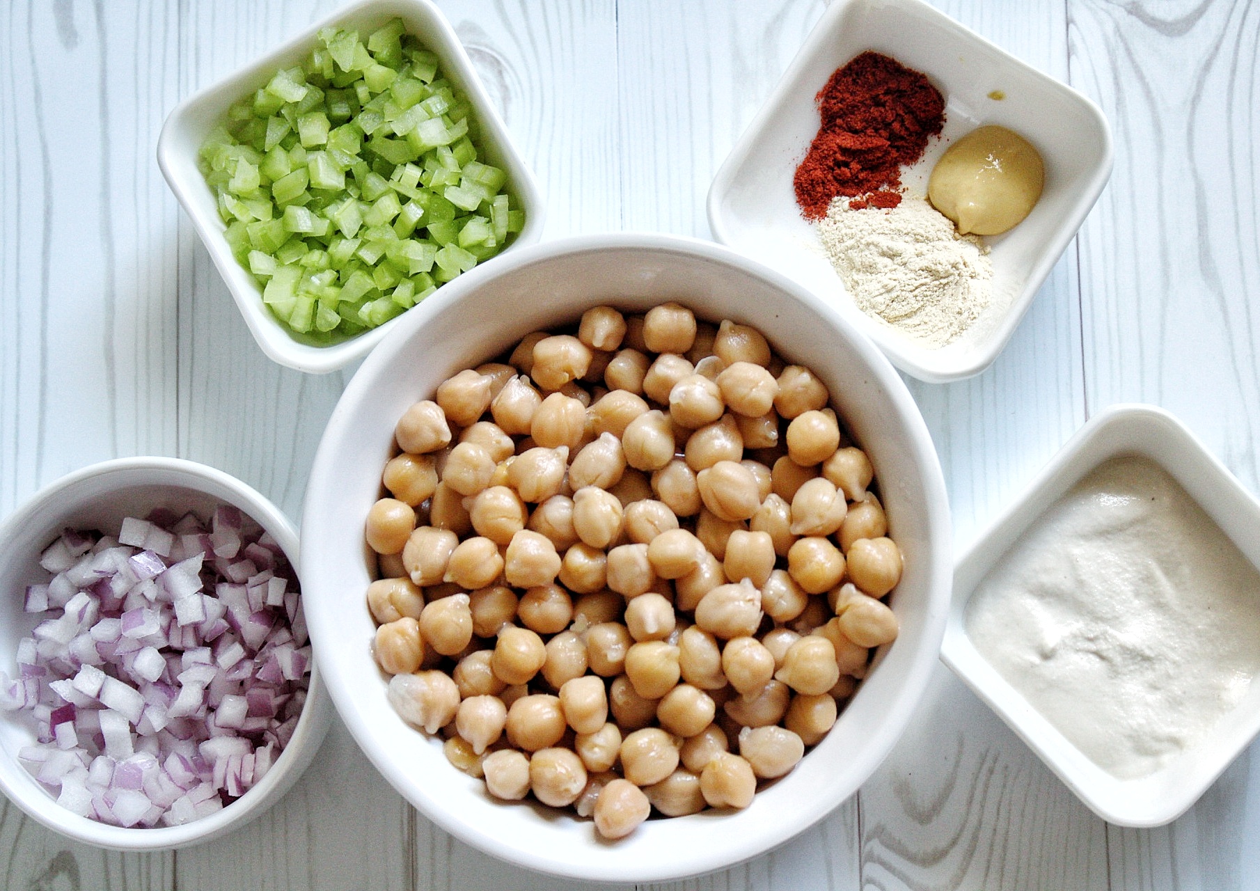 Ingredients for chickpea salad including spices, dijon mustard, cashew crea, onion, cucumber, and cooked chickpeas. 