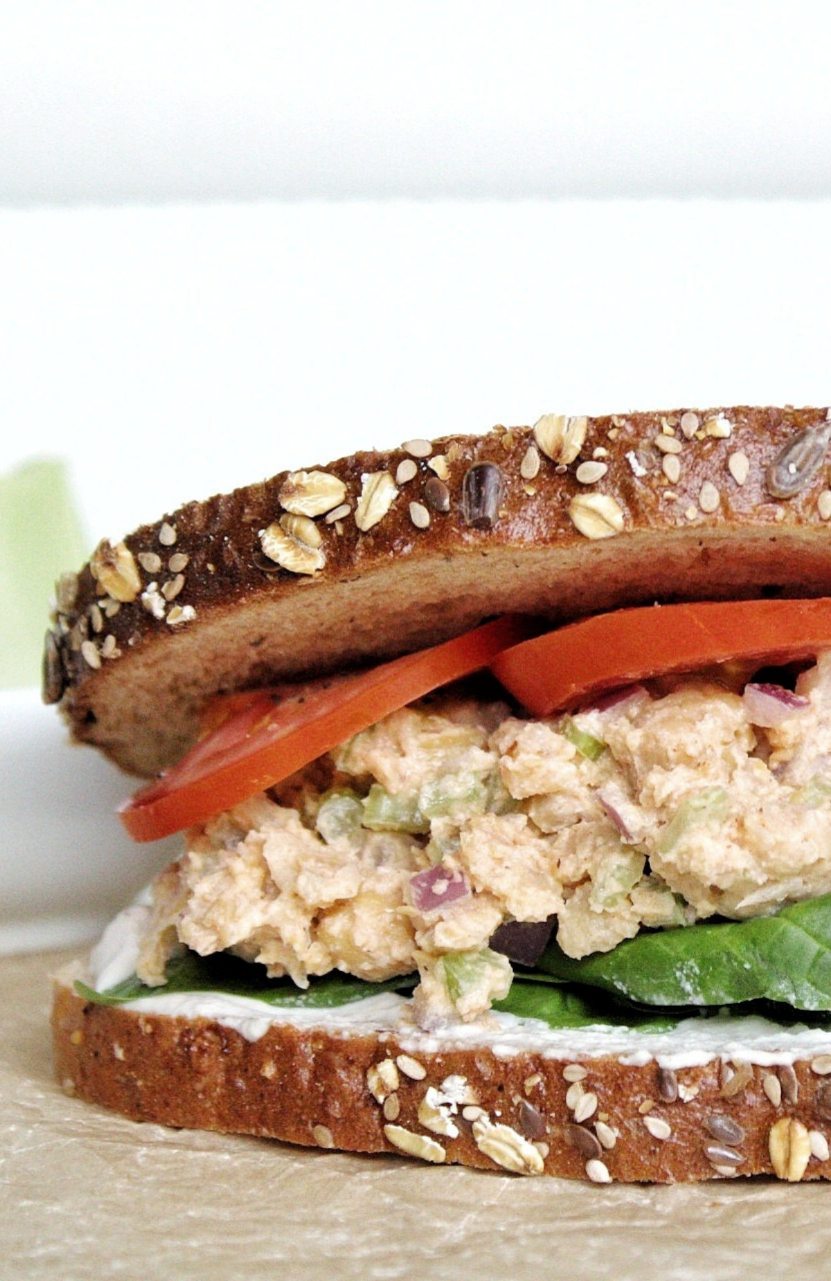 Closeup of chickpea salad sandwich with spinach, cashew cream, and sliced tomatoes. 