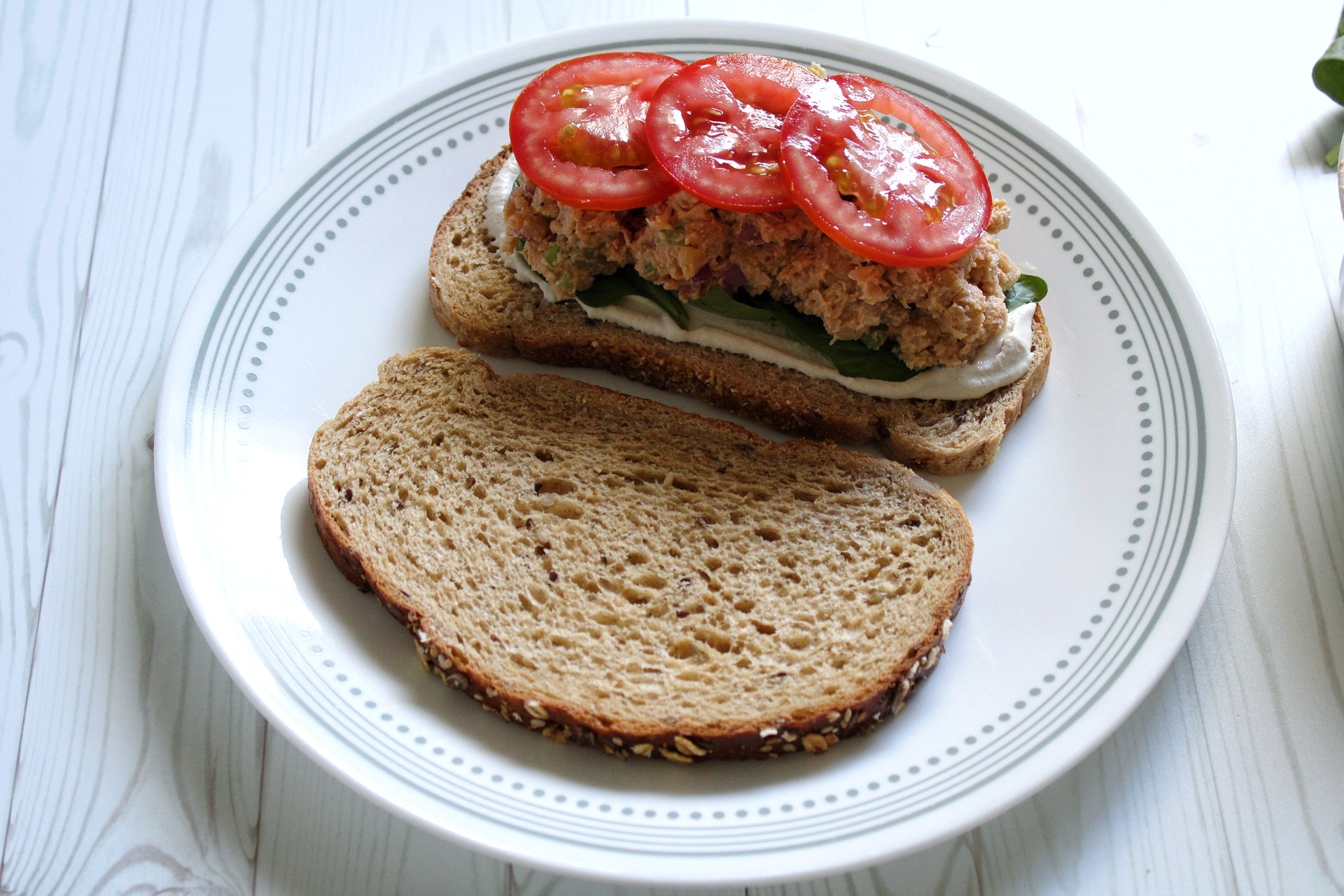 Open face chickpea salad sandwich on a plate topped with sliced tomatotes. 