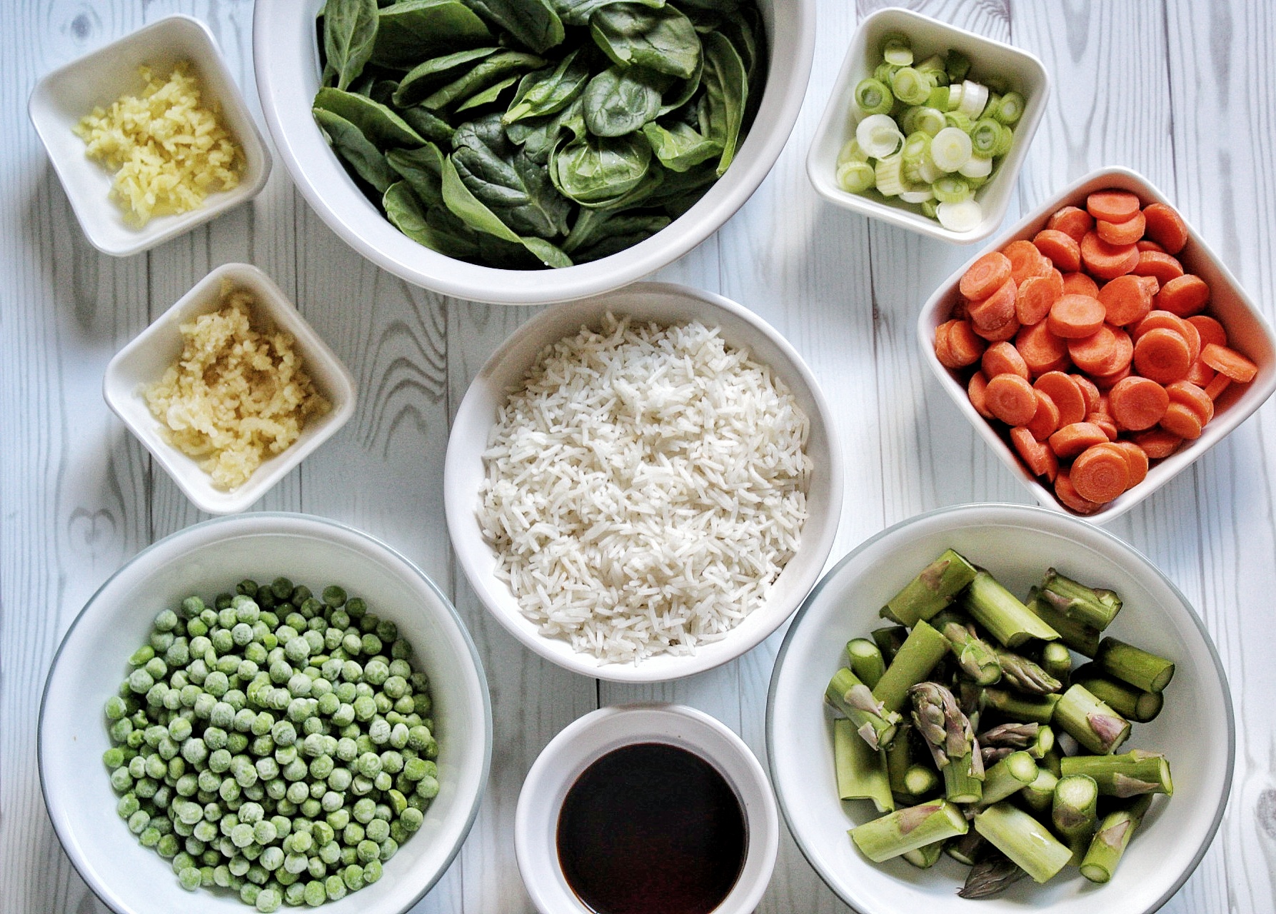 Spinach, green onions, carrots, asparagus, soy sauce, rice, green peas, garlic, and ginger in small bowls 