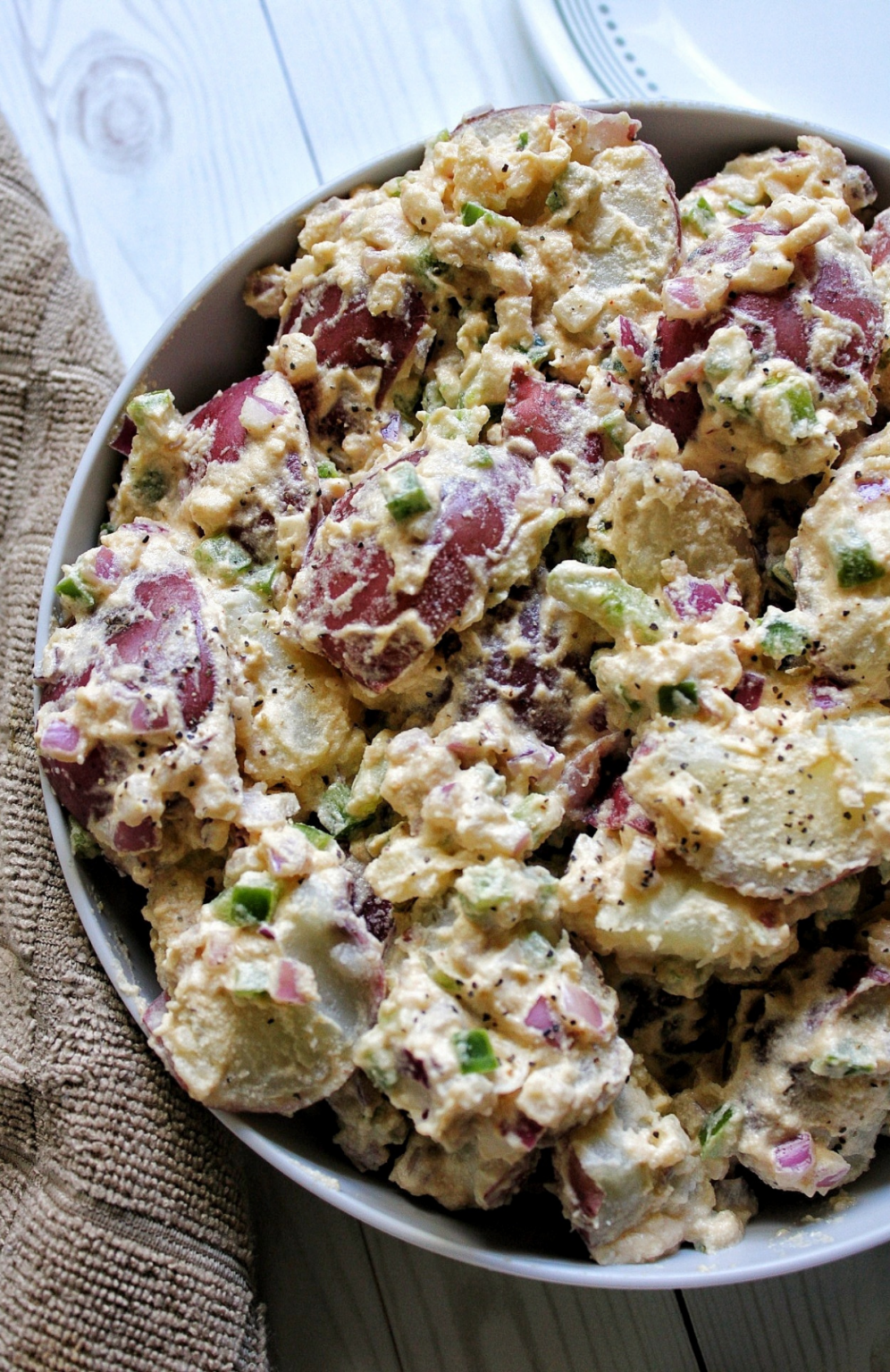 Potato salad made with red potatoes, cashew "mayo," onion, and bell pepper. Served in a gray bowl. 