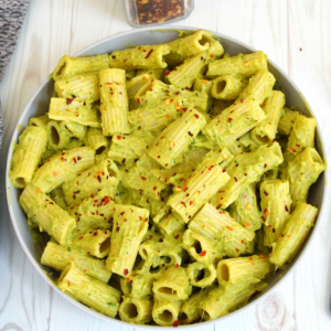 Rigatoni pasta in a creamy avocado sauce in a gray bowl. Topped with chili flakes.