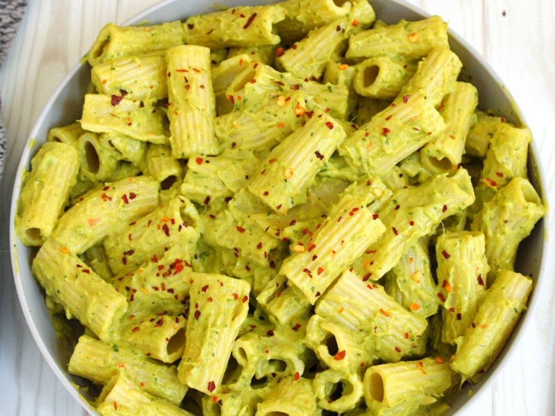 Rigatoni pasta in a creamy avocado sauce in a gray bowl. Topped with chili flakes.
