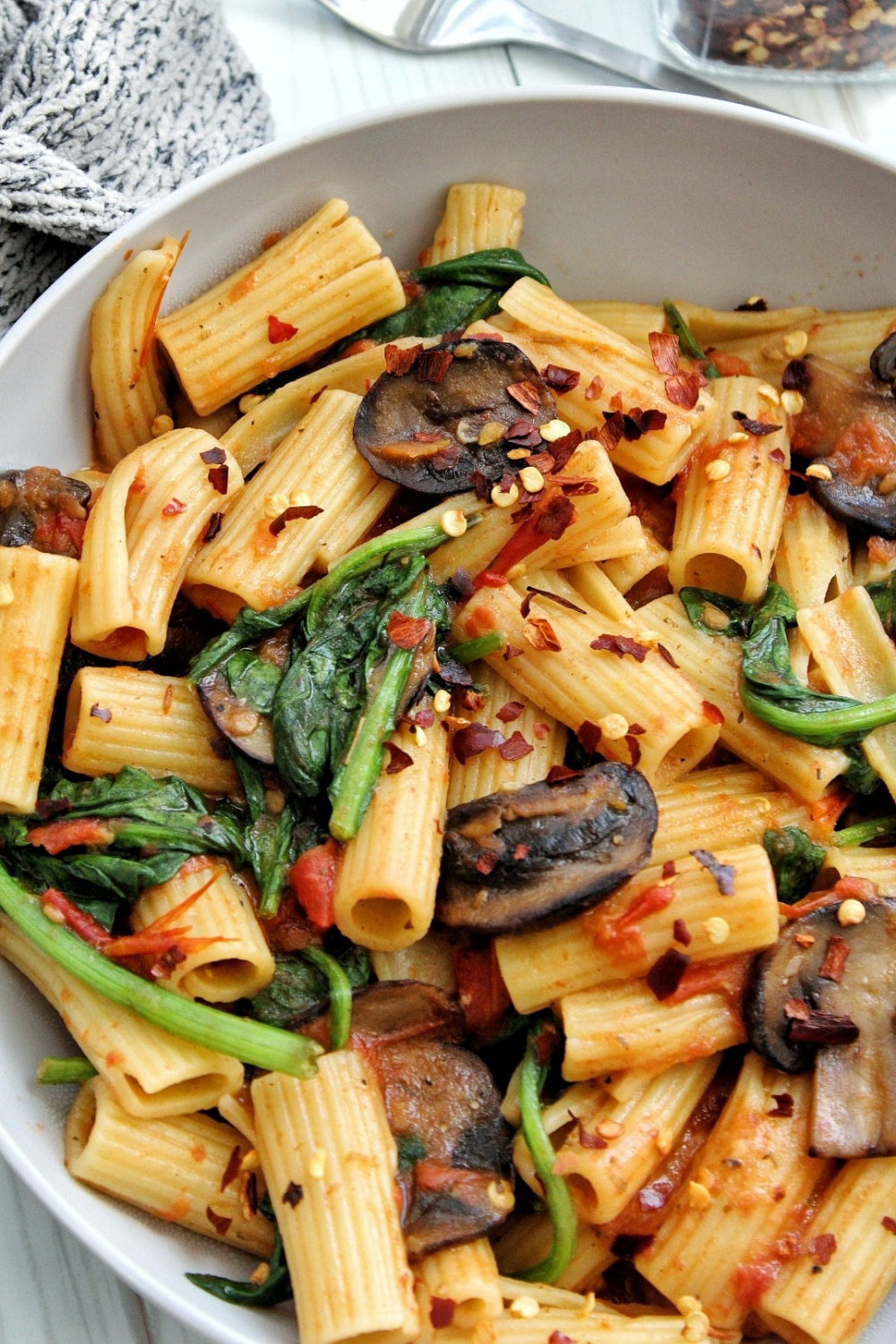 Closeup rigatoni pasta with mushrooms, spinach, and red chili flakes