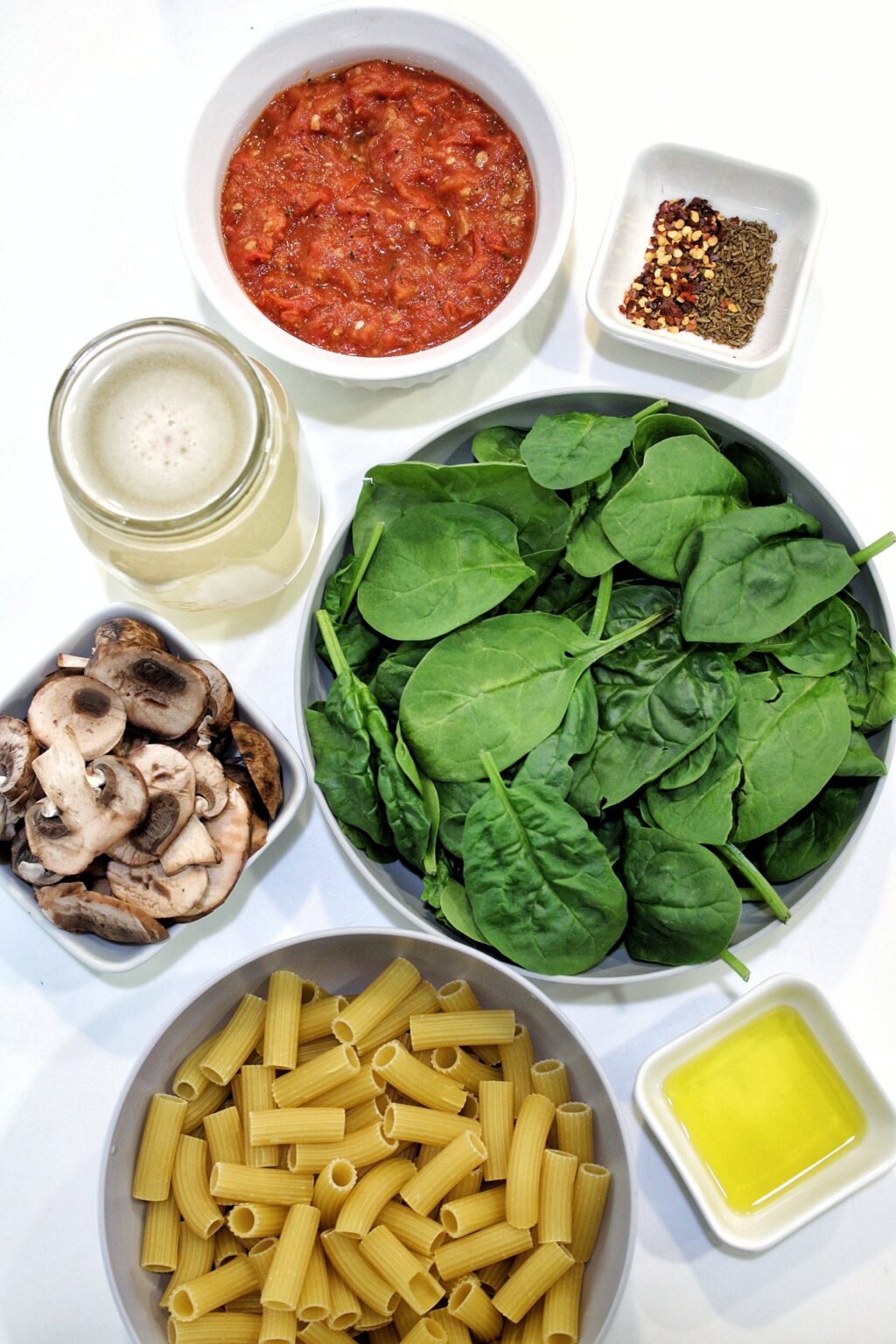 One-pot pasta ingredients: spinach, sliced mushrooms, mushroom broth, rigatoni pasta, olive oil, roasted tomatoes, spices