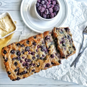 Blueberry banana bread with a bowl of frozen berries and vegan butter