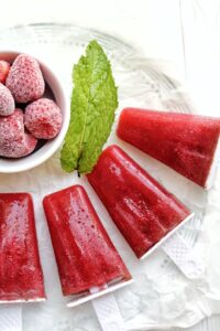 Sugar-free strawberry mint popsicles with a bowl of frozen strawberries