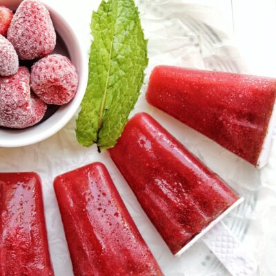 Sugar-free strawberry mint popsicles with a bowl of frozen strawberries