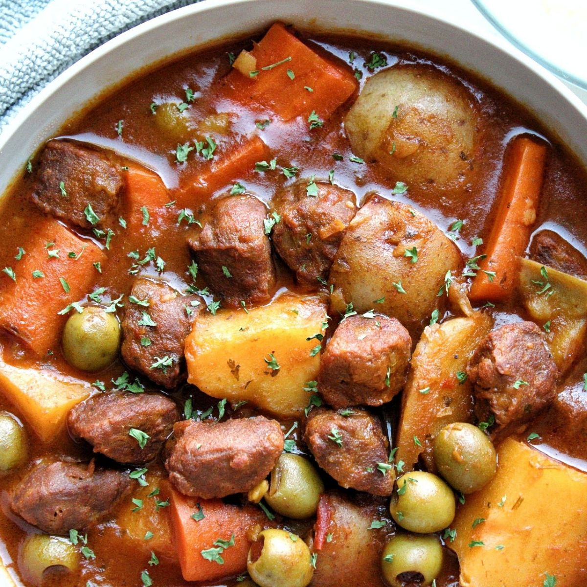 Vegetarian beef stew with chunks of potatoes, carrots, vegan beef, green olives in a gray bowl