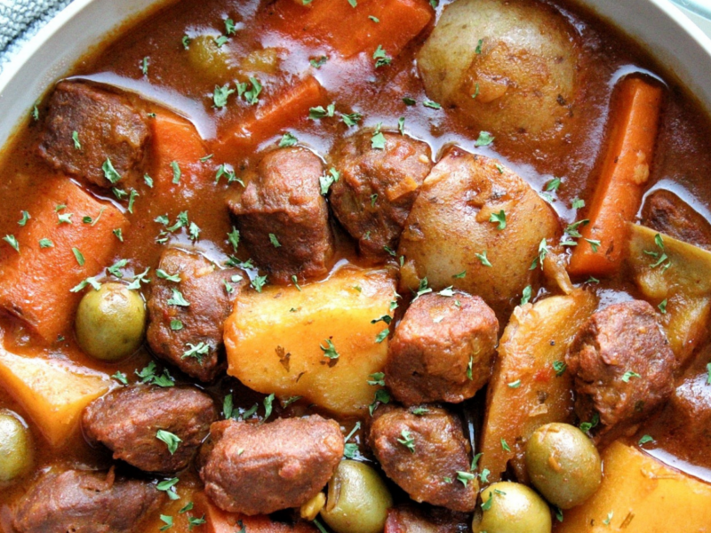 Vegetarian beef stew with chunks of potatoes, carrots, vegan beef, green olives in a gray bowl