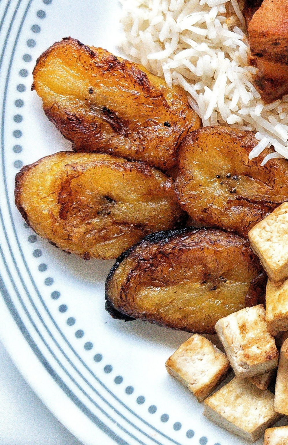 Sweet plantains on a plate with tofu and rice. 