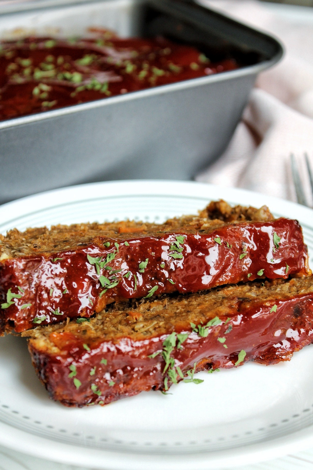 Two slices of vegan lentil loaf with ketchup glaze and topped with parsley. 