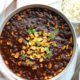 Vegan black bean chili in gray bowl topped with pan-roasted corn and chopped cilantro.