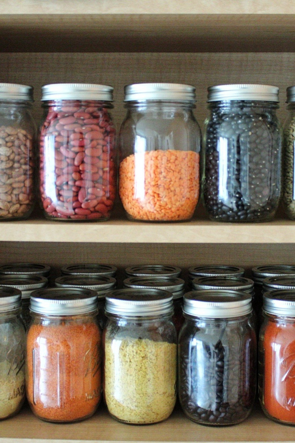 Mason jars filled with seasonings, spices, and dry legumes in a kitchen pantry 