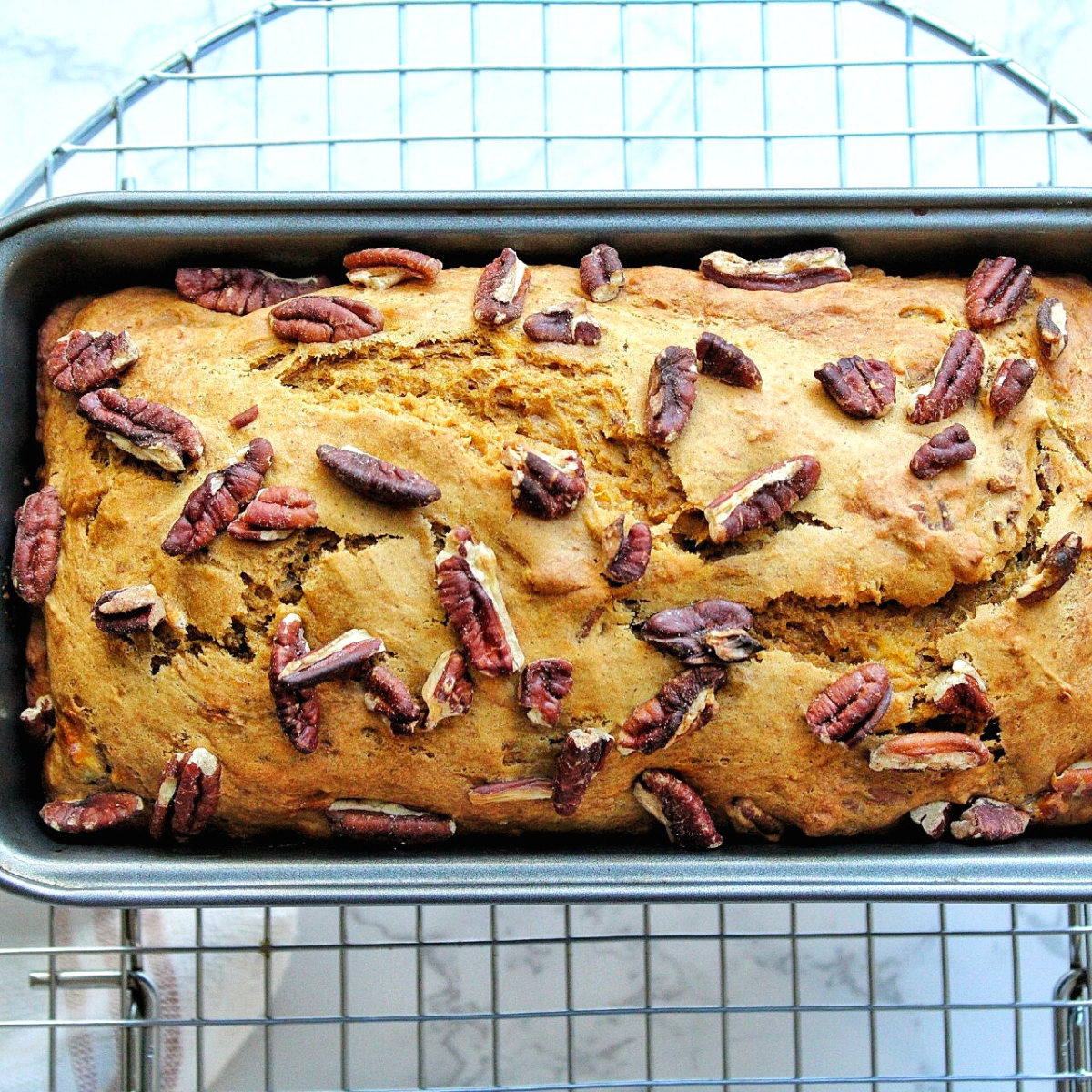 Pumpkin banana bread topped with pecans on a cooling rack. 