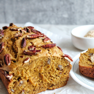 Loaf of pumpkin banana bread topped with choppedpecans with a slice on the side.