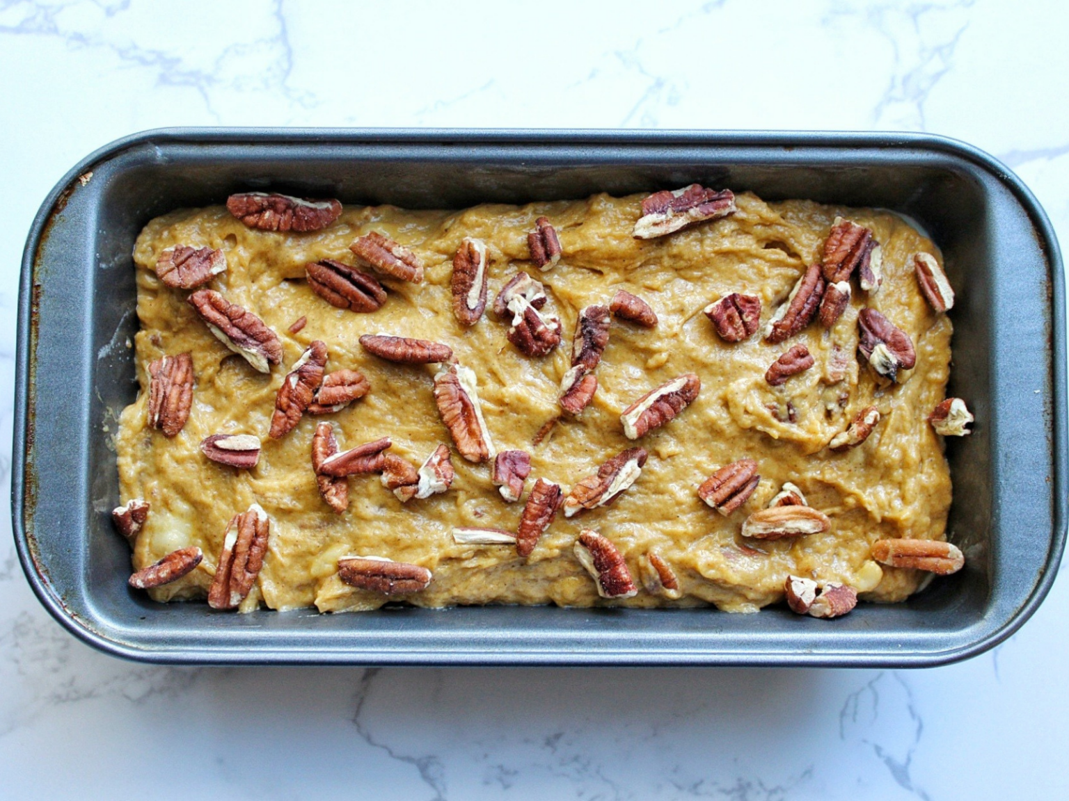 Unbaked or raw sweet cook bread in a loaf pan topped with chopped pecans. 