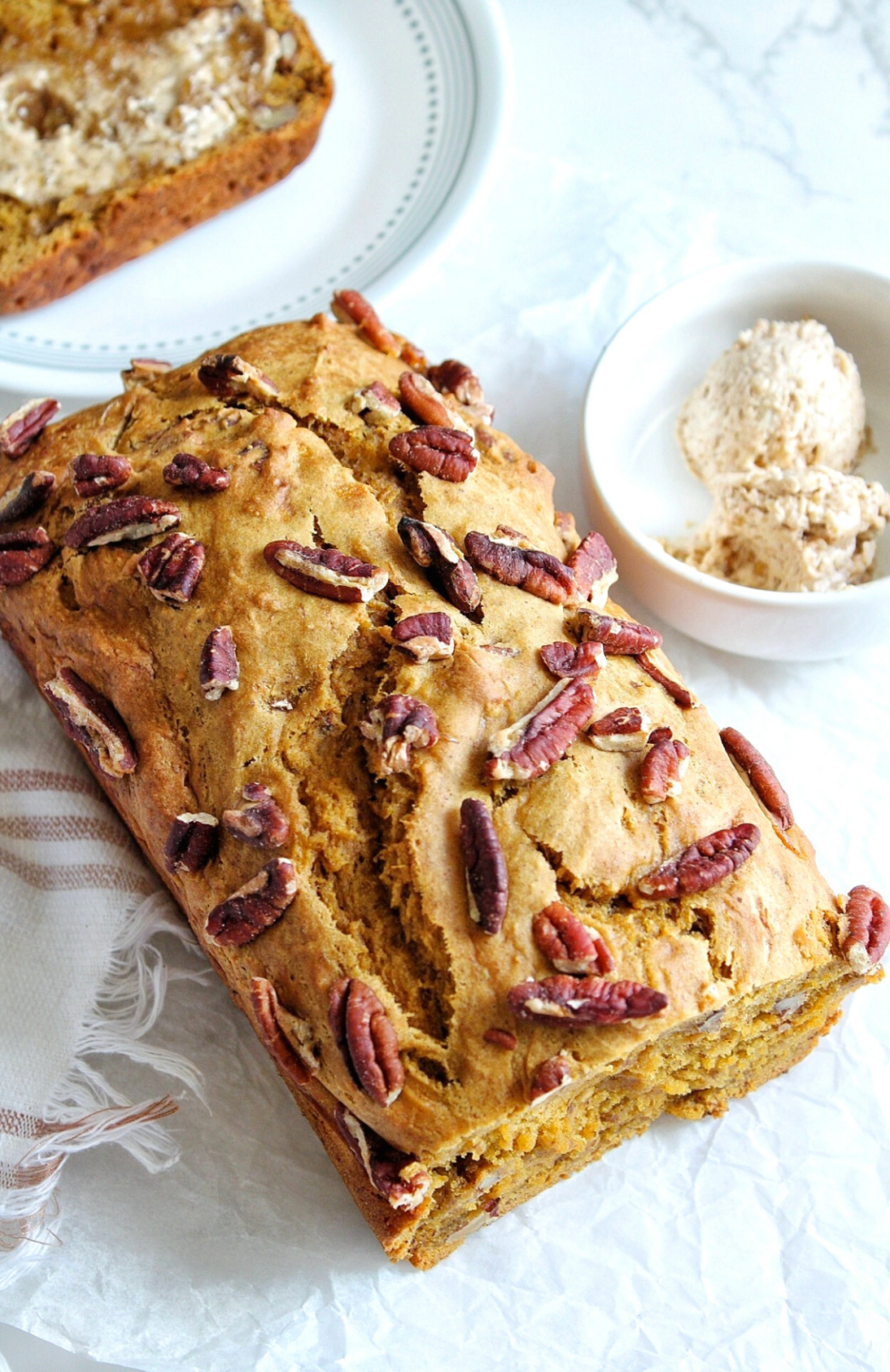 Loaf of pumpkin banana bread topped with chopped pecans and a small bowl with cinnamon brown sugar butter.