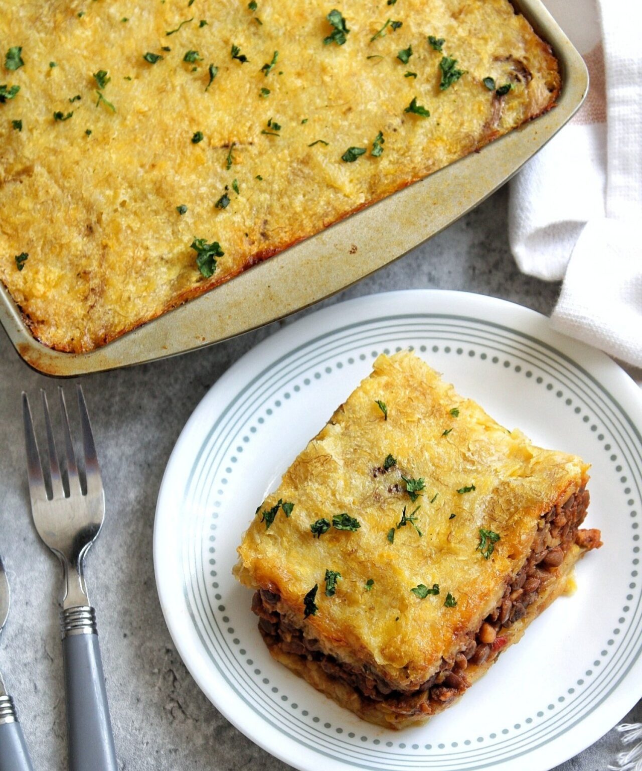 Slice of vegan pastelón de plátano maduro with the casserole showing in the back. 