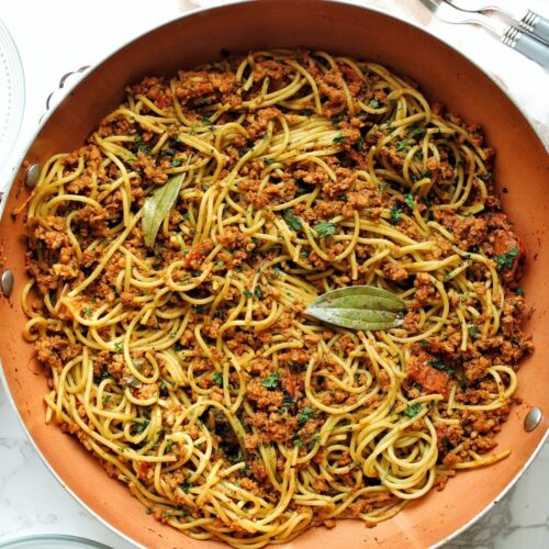 Finished Puerto Rican spaghetti in a large pot with bay leaves.