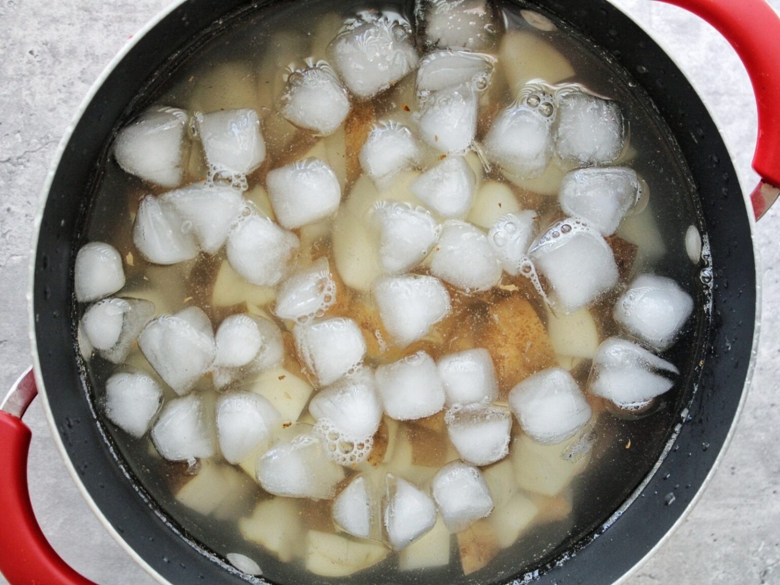 Chopeped russet potatoes in a large pot with ice cold water.