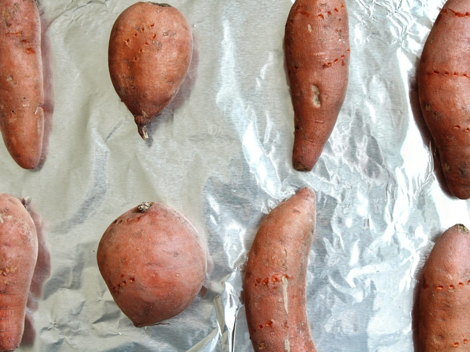 Uncooked sweet potatoes on a baking sheetlined with aluminum foil.