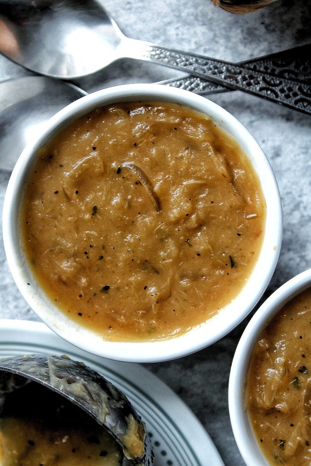 Closeup of onion gravy in a white bowl with spoons. 