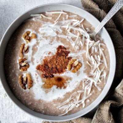 Homemade cream of rice in a gray bowl topped with a splash of coconut milk, nuts, cinamon, and cinnamon flakes.