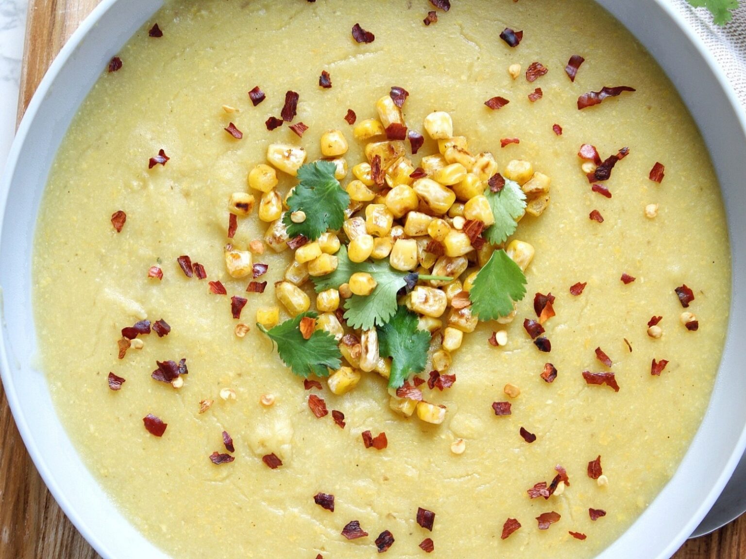 Gray bowl with creamy vegan corn soup topped with cilantro.