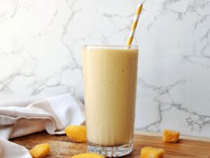 Peach mango smoothie in a glass cup with a yellow-stripped straw.