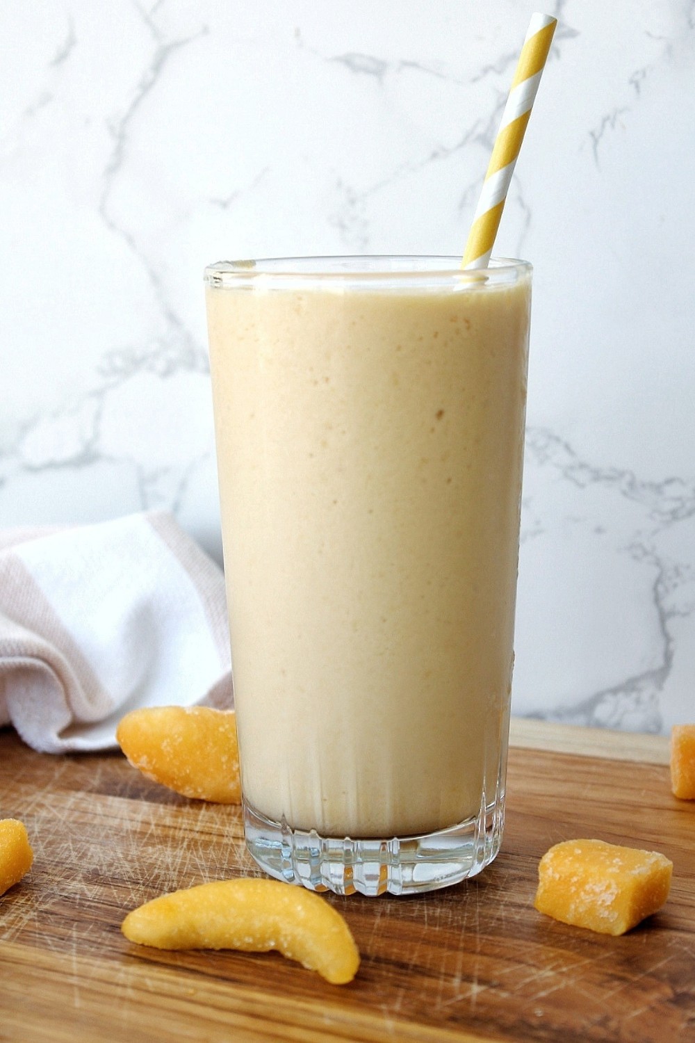 Close up of peach mango smoothie in a clear glasss cup and yellow-stripped straw.