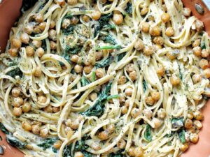 Linguine pasta with chickpeas, spinach, and coconut milk in a wok.