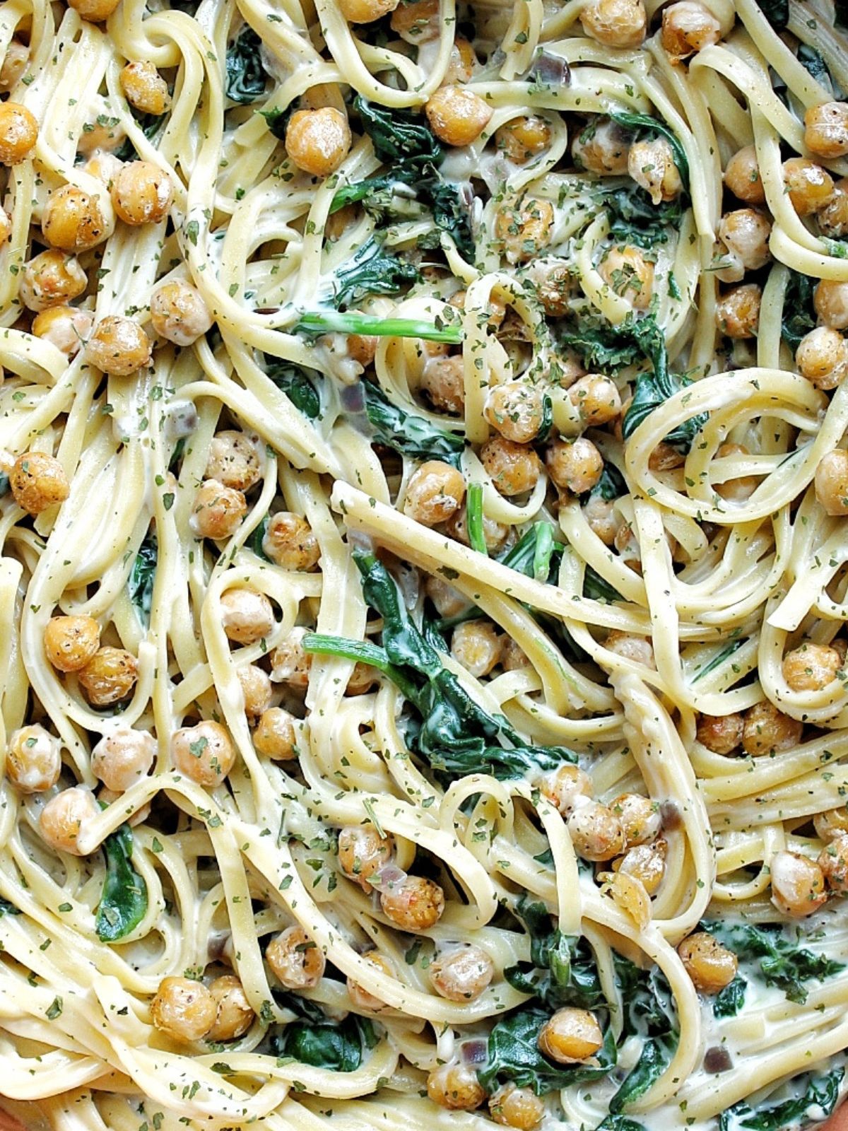 Closeup of creamy chickpea pasta with spinach. Topped with chopped herbs. 