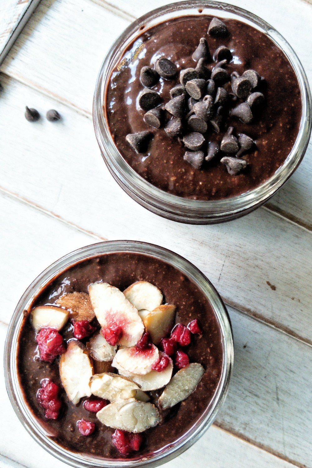 Chocolate chia pudding topped with chocolate chips. Another topped with sliced almonds and raspberries. 