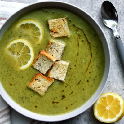 Zucchini soup in a bowl topped with lemon slices and homemade croutons.